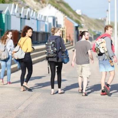 Group pf people walking along a promenade with beach huts in the background